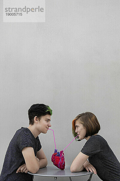 Teenage couple drinking from heart against gray background