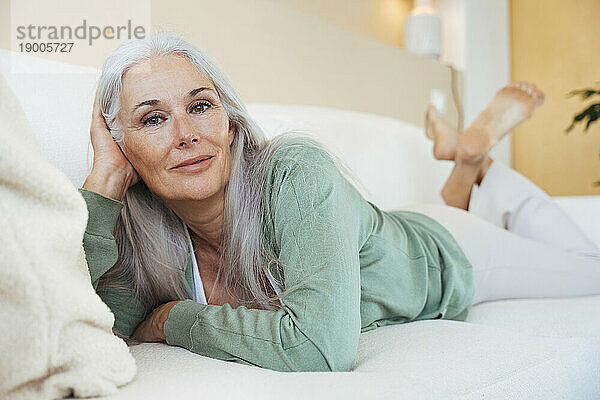 Lächelnde reife Frau entspannt sich zu Hause auf dem Sofa
