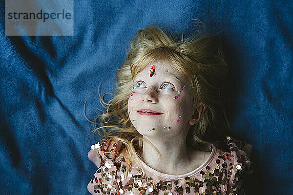 Happy girl with crystals on face lying on blue fabric
