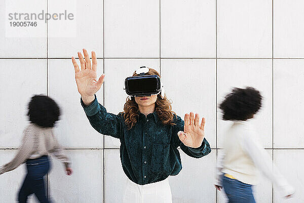 Businesswoman wearing virtual reality simulators gesturing in front of wall