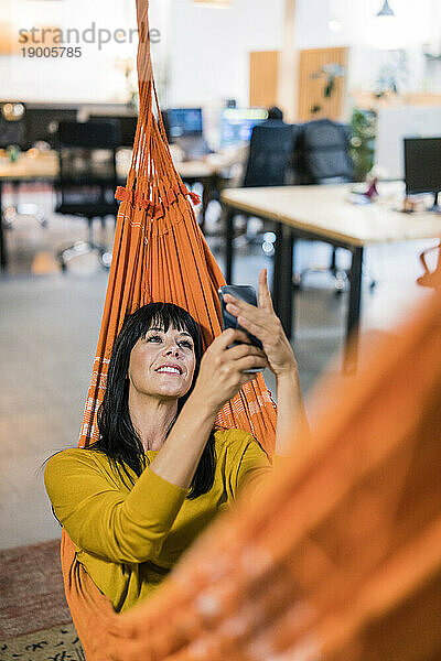 Lächelnde Geschäftsfrau benutzt Smartphone und entspannt in der Hängematte