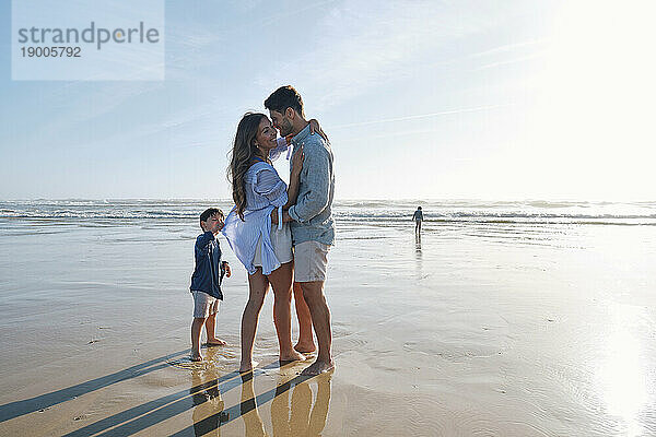 Junge steht mit romantischen Eltern und tanzt am Strand