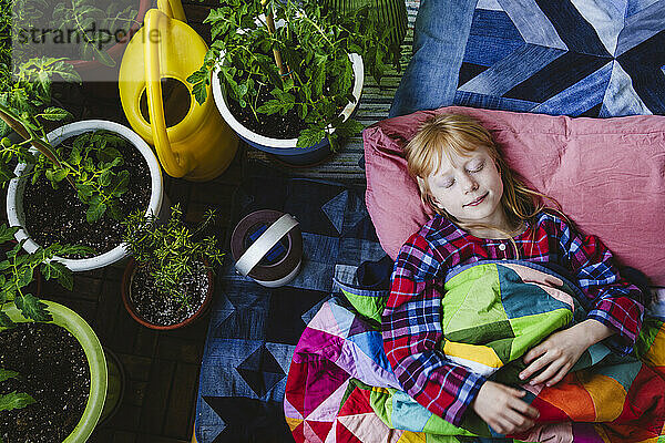 Mädchen schläft mit Decke neben Pflanzen auf dem Balkon