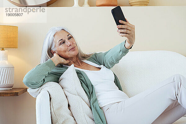 Lächelnde reife Frau  die zu Hause ein Selfie mit dem Mobiltelefon macht