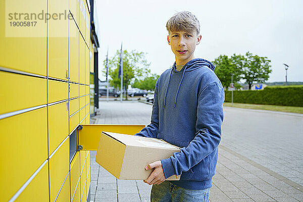 Junge mit Paket steht am gelben Paketschließfach