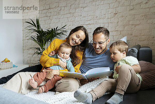 Happy parents reading book for children on couch at home
