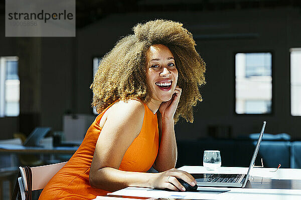 Glückliche Geschäftsfrau sitzt mit Laptop am Schreibtisch