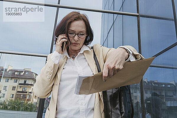 Geschäftsfrau spricht am Smartphone und hält Dokumente in der Hand