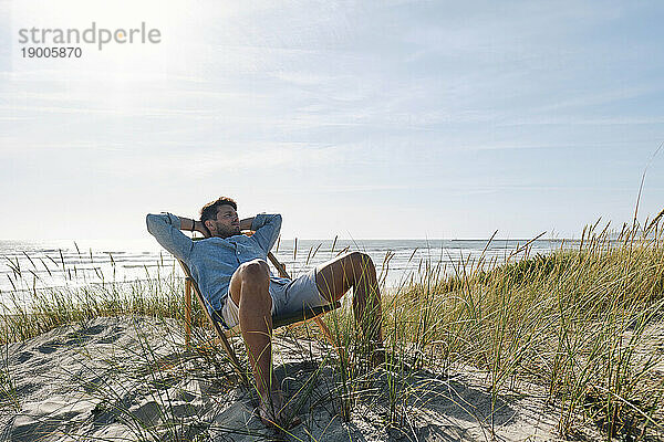 Mann entspannt sich an einem sonnigen Tag auf einem Stuhl am Strand