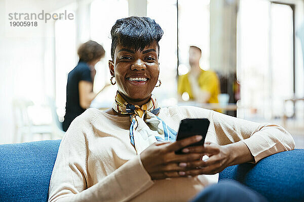 Glücklich lächelnde Geschäftsfrau  die mit Mobiltelefon im Büro sitzt