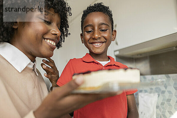 Glücklicher Junge mit Mutter  die zu Hause Kuchen in der Küche hält
