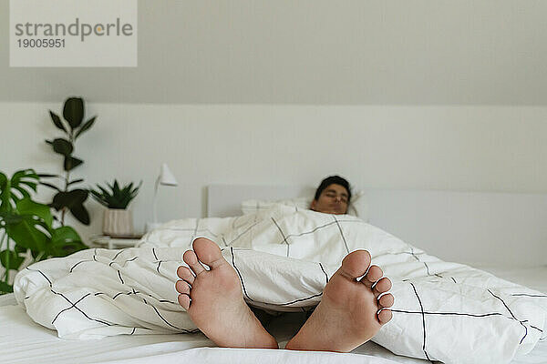 Junger Mann ruht sich barfuß zu Hause im Bett aus