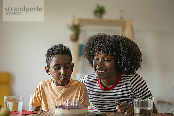 Glückliche Mutter mit ihrem Sohn  der zu Hause Kerzen auf den Kuchen bläst