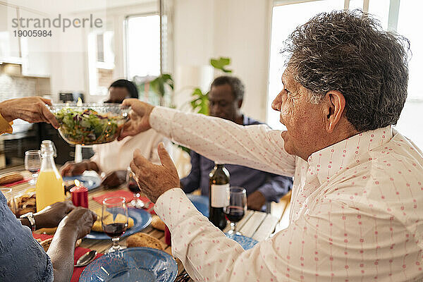 Älterer Mann reicht einem Freund zu Hause eine Salatschüssel