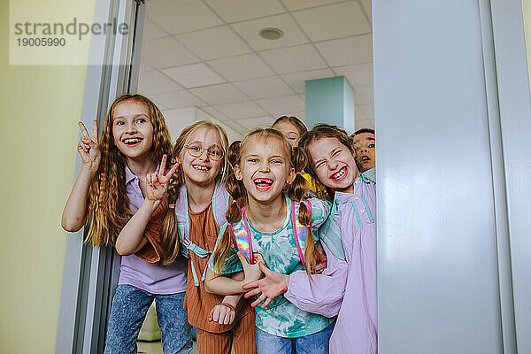 Happy school children gesturing standing in classroom doorway
