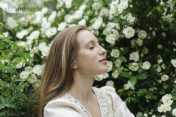 Young woman with eyes closed by white flower bush
