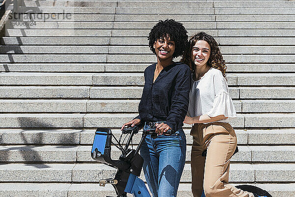 Fröhliche junge Freunde mit Elektrofahrrad stehen vor der Treppe