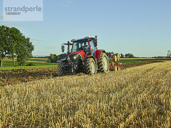 Landwirt benutzt Traktor und pflügt bei Sonnenaufgang Land in der Nähe von trockenem Gras