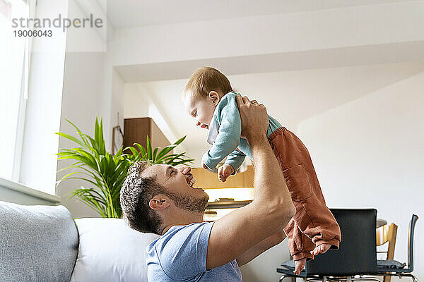 Vater hebt niedlichen kleinen Jungen im heimischen Wohnzimmer hoch