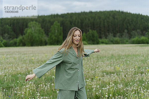 Carefree young woman with arms outstretched walking on dandelion field