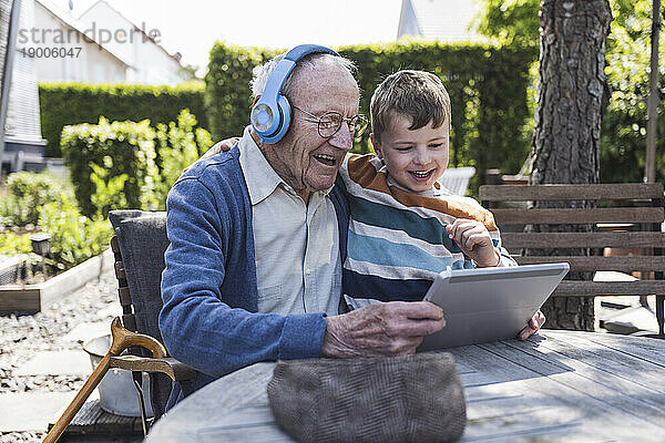 Glücklicher älterer Mann mit kabellosen Kopfhörern und Tablet-PC mit Enkel