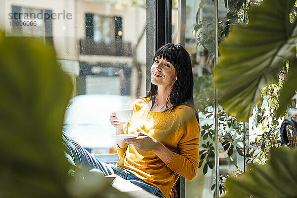 Lächelnde Frau sitzt mit Kaffeetasse im Café