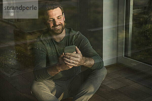 Glücklicher Mann benutzt Mobiltelefon  gesehen durch Glas