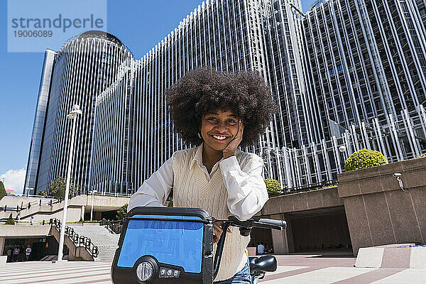 Glückliche junge Geschäftsfrau steht mit Elektrofahrrad im Büropark