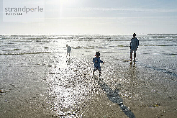 Vater genießt mit Kindern am Strand an einem sonnigen Tag