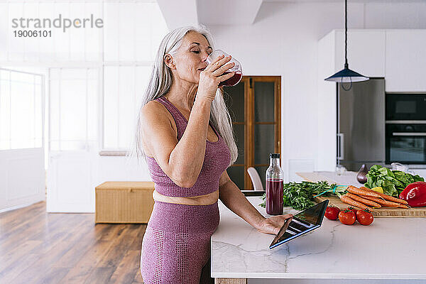 Reife Frau mit Tablet-PC trinkt zu Hause Saft