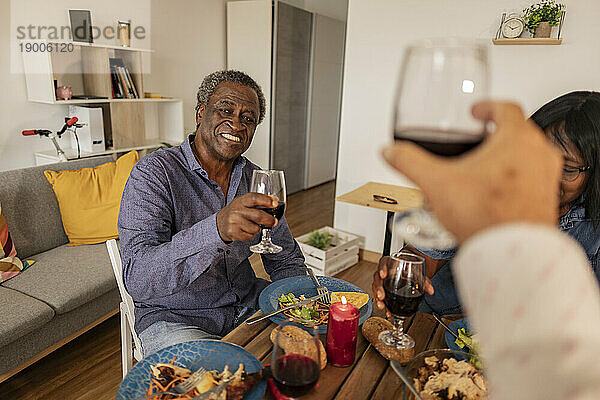 Lächelnder älterer Mann  der mit Freunden bei einer Dinnerparty Wein genießt