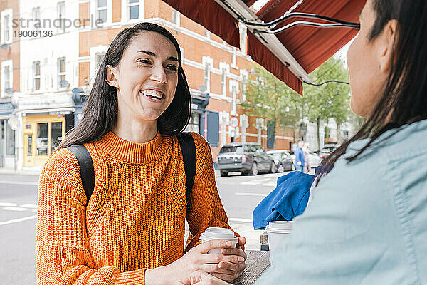 Lächelnde Freunde reden und trinken Kaffee im Straßencafé