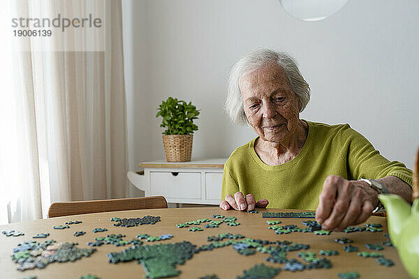 Elderly woman solving jigsaw puzzle on table