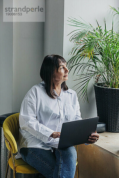 Nachdenkliche Frau sitzt mit Laptop auf einem Stuhl