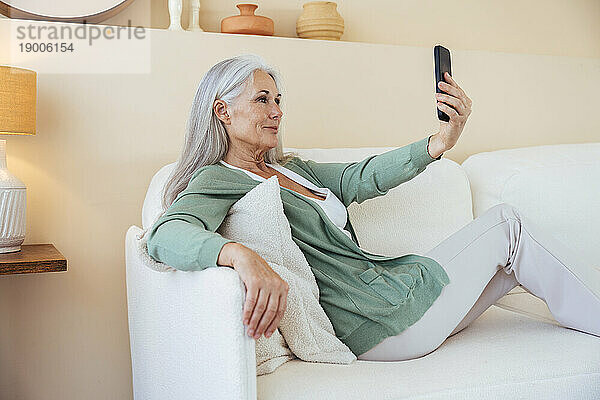 Lächelnde reife Frau  die zu Hause ein Selfie mit dem Smartphone macht