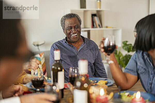 Glücklicher älterer Mann  der mit einem Freund spricht  der zu Hause ein Weinglas hält