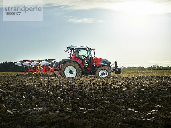 Farmer plowing field using tractor at sunrise