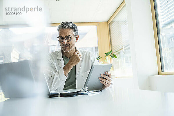 Reifer Mann im Laborkittel mit Tablet-PC in der Klinik