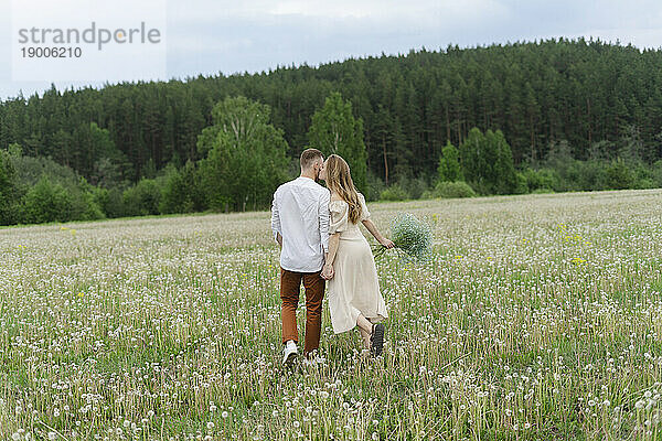 Young couple kissing walking on wildflower field