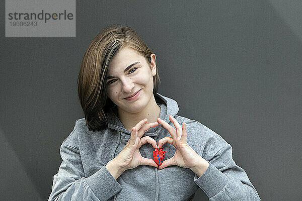 Teenager-Mädchen gestikuliert mit Model-Herz vor grauem Hintergrund