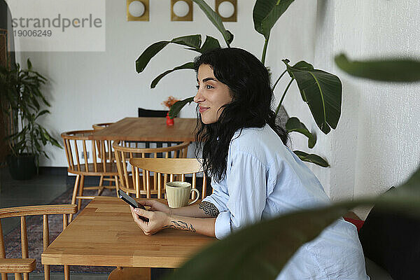 Nachdenkliche Frau sitzt mit Smartphone im Café