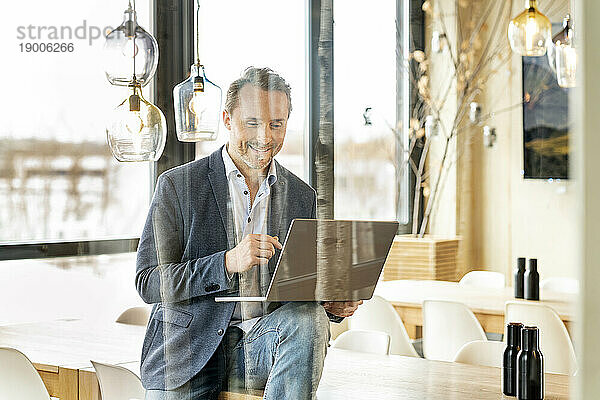 Lächelnder Geschäftsmann mit Laptop durch Glas gesehen
