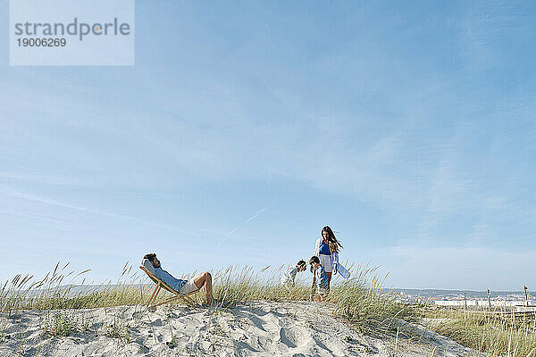 Vater entspannt sich auf Stuhl mit Familie und verbringt Freizeit am Strand