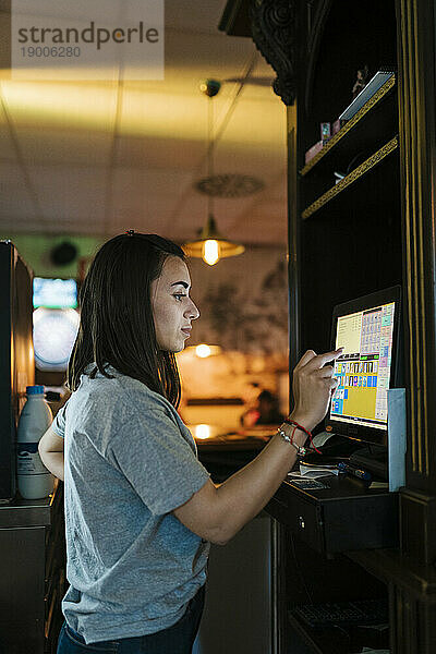 Junge Kassiererin bedient Touchscreen-Computer an der Bar