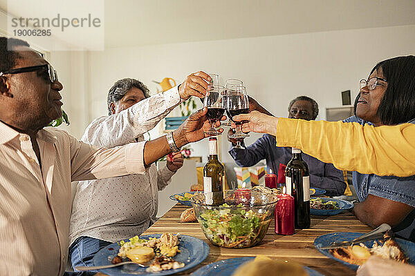 Multikulturelle ältere Freunde feiern mit Wein am Esstisch