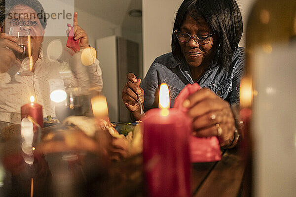 Lächelnde ältere Frau  die zu Hause Essen mit Kerzen auf dem Tisch isst