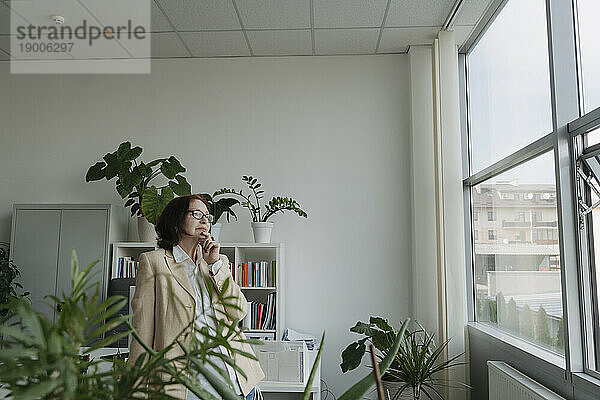 Nachdenkliche Geschäftsfrau blickt durch Glasfenster im Büro