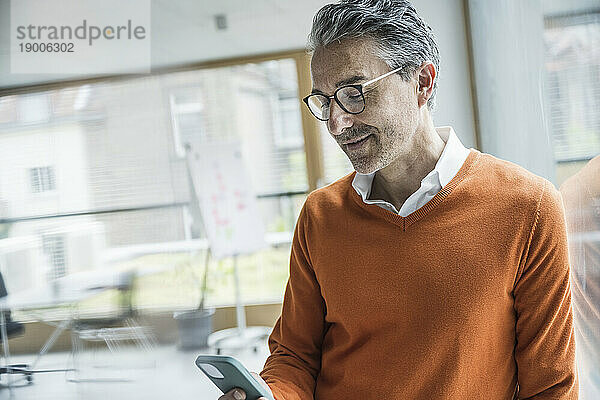Reifer Geschäftsmann nutzt Smartphone im Büro
