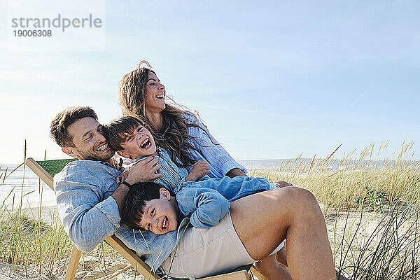 Glückliche Familie umarmt Vater auf Stuhl am Strand