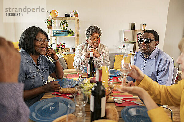 Multikulturelle ältere Freunde essen am Esstisch zu Hause zu Abend
